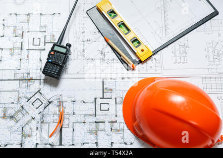 Orange hard hat, level meter, glasses and walkie talkie with blueprints on a table. Architectural and construction concept Stock Photo