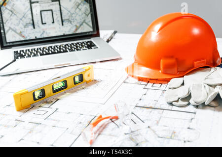 Orange hard hat, laptop  with drawings, level meter, glasses and gloves lying on a  blueprints on a table. Architectural and construction concept Stock Photo
