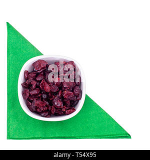 Dried red cranberries in a bowl on green serviette, napkin isolated on white, top view. Stock Photo