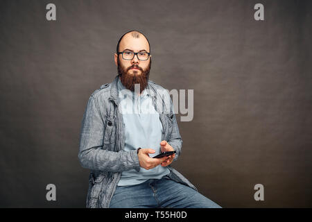 bearded man in glasses with phone in hand on brown background. Stock Photo