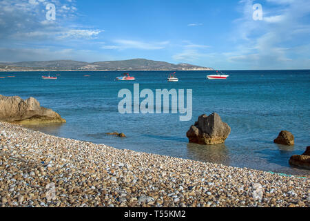 Crystal clear sea with rocks on a pebble beach foreground under blue skies Stock Photo