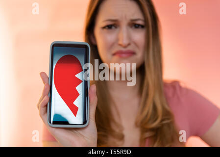Young woman holding smart phone displaying broken heart Stock Photo