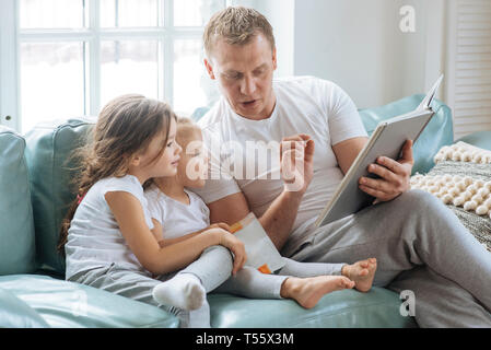 Father reading book to daughters on sofa Stock Photo