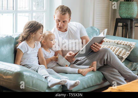 Father reading book to daughters on sofa Stock Photo