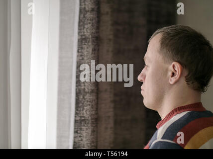 Pensive young man looks out the window, side view Stock Photo
