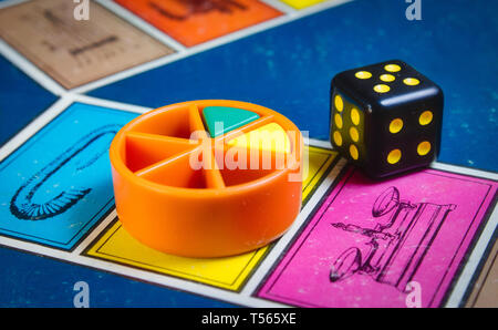 London, UK - 07 April 2019: Close-up of classic board game Trivial Pursuit with black die and colored plastic pieces of different colors Stock Photo