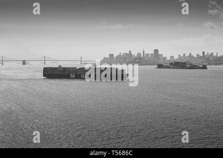 Black And White Photo Of Mediterranean Shipping Company Container Ship, MSC ARIANE, Steaming Through San Francisco Bay, San Francisco Skyline Behind. Stock Photo