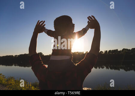 Young happy family with childrens having fun in nature. Little boy sitting on father's shoulders Stock Photo