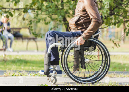 A young man in a wheelchair rides along the park road. Stock Photo