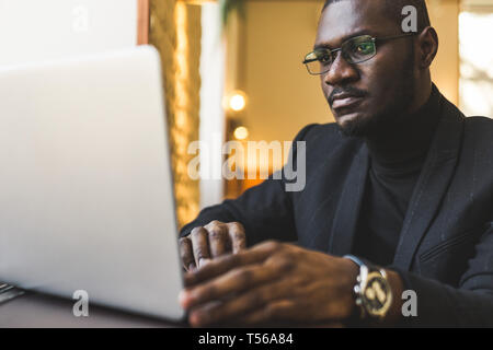Young handsome dark-skinned businessman in a cafe working behind a laptop with a cup of tea. Stock Photo