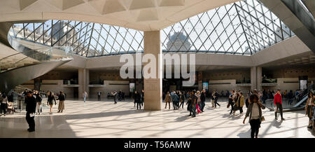 Paris, France - March 31, 2019: Visitors walking in the hall of Louvre Pyramid with following view of metal and glass ceiling Stock Photo