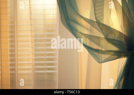 Sunny sunset light through the thin curtains on the window with blinds Stock Photo