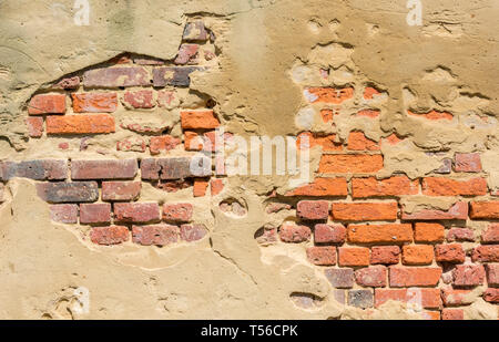 plaster or render on a wall flaking plastering and red bricks in need of repairs to mortar. Stock Photo