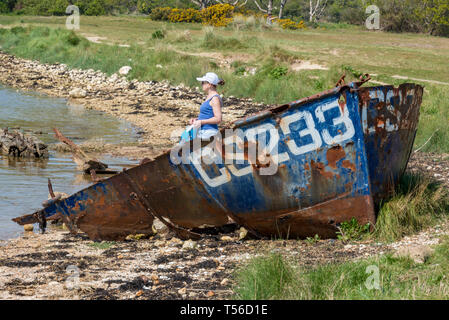 woman standing near an old shipwreck or derelict boat at the side of bembridge harbour on the isle of wight. Stock Photo