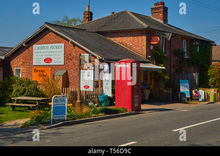 Red phone box outside store on the main road through Kent village of Penhurst, England, United Kingdom, Europe Stock Photo