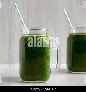 Green smoothie with spinach, avocado and banana in glass jars on a white wooden surface, side view. Close-up. Stock Photo