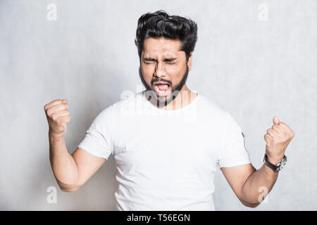 Portrait of overjoyed man clenches fists with happiness, poses against white background. Stock Photo