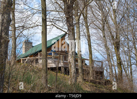 rustic cabin with wooden deck and green roof on a hill in spring woods Stock Photo