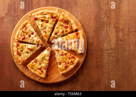 Slices of a cut quiche pie, shot from the top on a dark rustic wooden background with a place for text Stock Photo