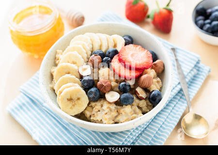 Oatmeal porridge with honey, fruits and berries in bowl on blue napkin. Closeup view Stock Photo