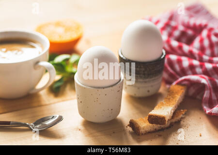 Boiled eggs for breakfast, cup of coffee, toasted bread and orange half. Healthy tasty breakfast on a wooden table. Closeup view, selective focus, ton Stock Photo