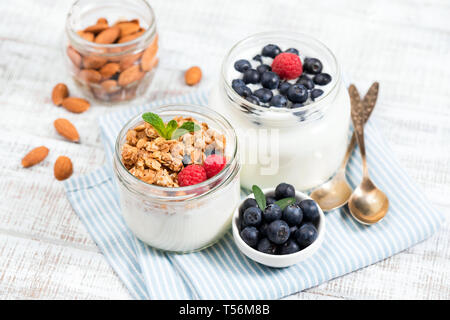 Jar of greek yogurt with granola and berries on white wooden background. Healthy eating, clean eating, dieting concept Stock Photo