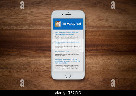 An iPhone showing The Motley Fool website rests on a plain wooden table (Editorial use only). Stock Photo