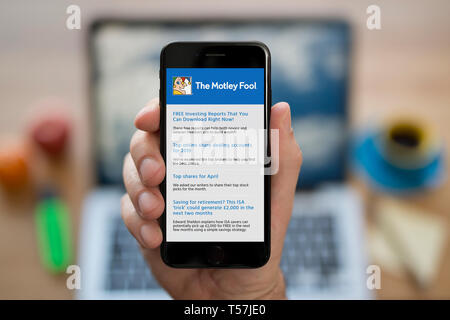 A man looks at his iPhone which displays The Motley Fool logo (Editorial use only). Stock Photo