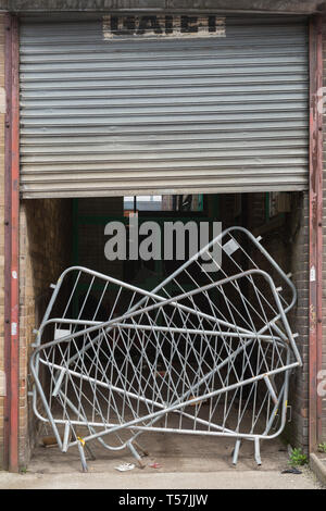 Stacked metal barriers across factory entrance with half closed metal roller shutter above Stock Photo