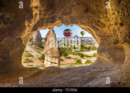 Hand carved arch in limestone rock in Goreme National Park, Cappadocia. Colorful hot air balloons flies in blue sky in Kapadokya, Turkey Stock Photo