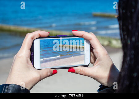 young woman using a mobile smartphone to take photo of the sea on sunny day closeup Stock Photo