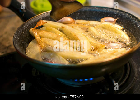 Frying fries and garlic in oil boiling beautifully on old cast iron pan. Cooking fry potatoes in pan in Spain,2019. Stock Photo
