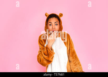 Young woman in bunny kigurumi standing isolated on pink background looking camera covering mouth shocked Stock Photo