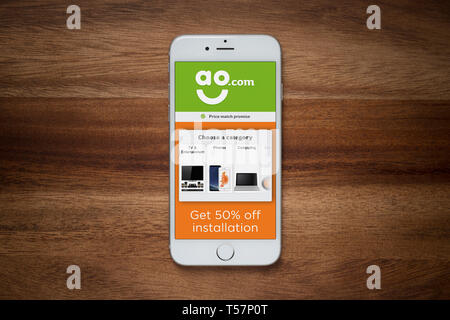 An iPhone showing the ao.com website rests on a plain wooden table (Editorial use only). Stock Photo