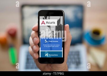 A man looks at his iPhone which displays the Acuris logo (Editorial use only). Stock Photo