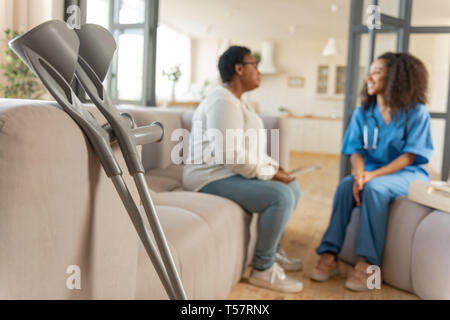 The pair of crutches standing near sofa with patient and nurse Stock Photo