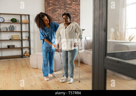 Woman making first steps with crutches standing near private nurse Stock Photo
