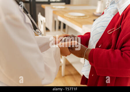 Woman wearing bracelet shaking hands of her caring caregiver Stock Photo