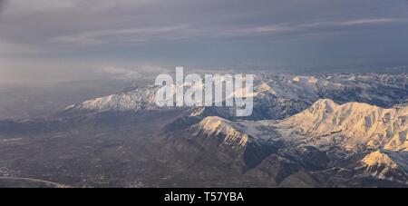 Aerial view from airplane of the Wasatch Front Rocky Mountain Range with snow capped peaks in winter including urban cities of Provo, Farmington Bount Stock Photo