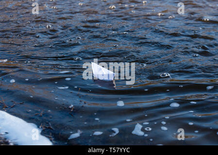 A paper boat on a turbulent stream of water struggles with the flow. Small paper boat is flowing along river Stock Photo