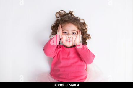 Beautiful little girl lies on the white floor and smile. Stock Photo