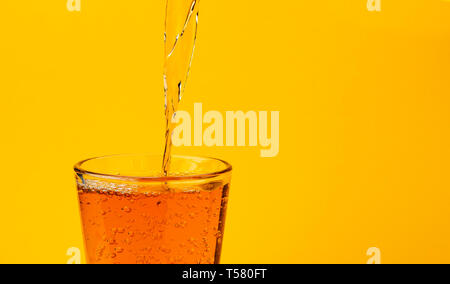 Apple juice pouring into glass, isolated on yellow background Stock Photo