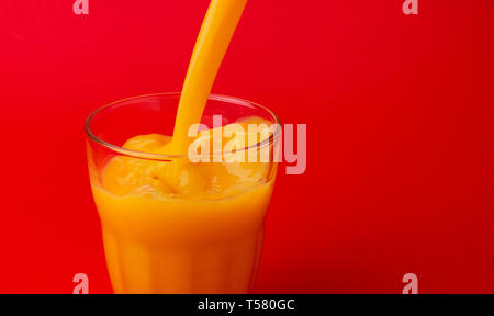 Orange juice pouring into glass, isolated on red background, with copy space Stock Photo