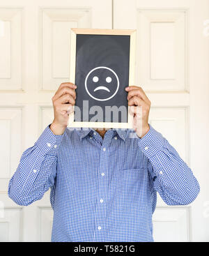 Sad unhappy face or depressed emotions concept, man had a board in front of his face with a sad emoticon on it Stock Photo