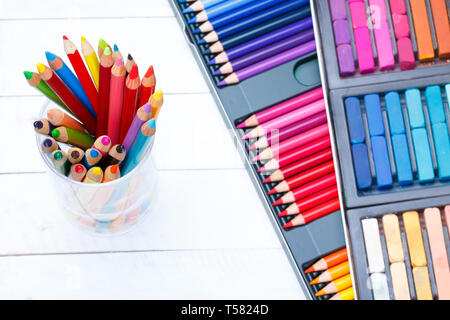 Multi colored pencils in jar on wooden table, with pastel and pencils box on background Stock Photo