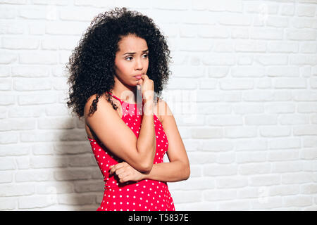 Portrait of worried african american woman against white wall. Black girl showing anxiety, impatience, sadness and frustration, biting nails. Stock Photo