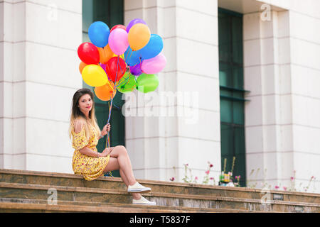 A woman are sitting down on stairs with ballons in her hands and smile. Stock Photo