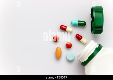 Multicoloured capsules with white medicine bottles and green caps on white background. Copy space for text or articles. Concepts of health and medicin Stock Photo