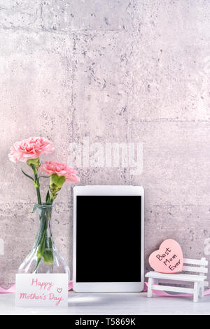Home decor with blooming carnation and tablet as photo frame beside wall on the table - Close up, copy space, mock up, beautiful mothers day concept. Stock Photo