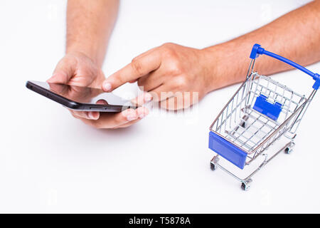 cropped man hands holding a smart phone beside a Mini shopping trolley - online shopping concept Stock Photo